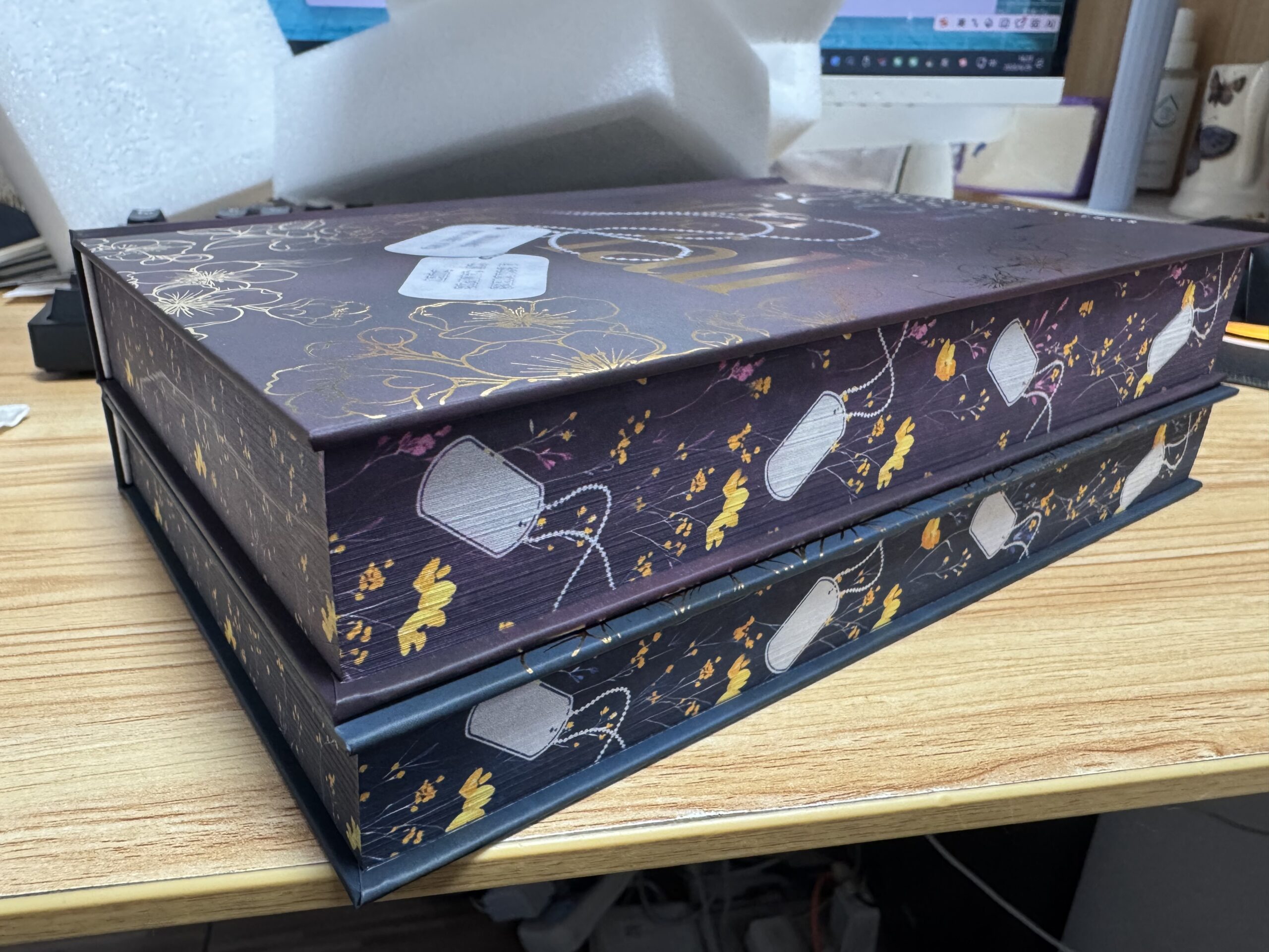 hardcover edges of Welcome to the Fall and After the Fall special edition. deep mauve and deep blue covers with gold letters and dog tags among flowers. 