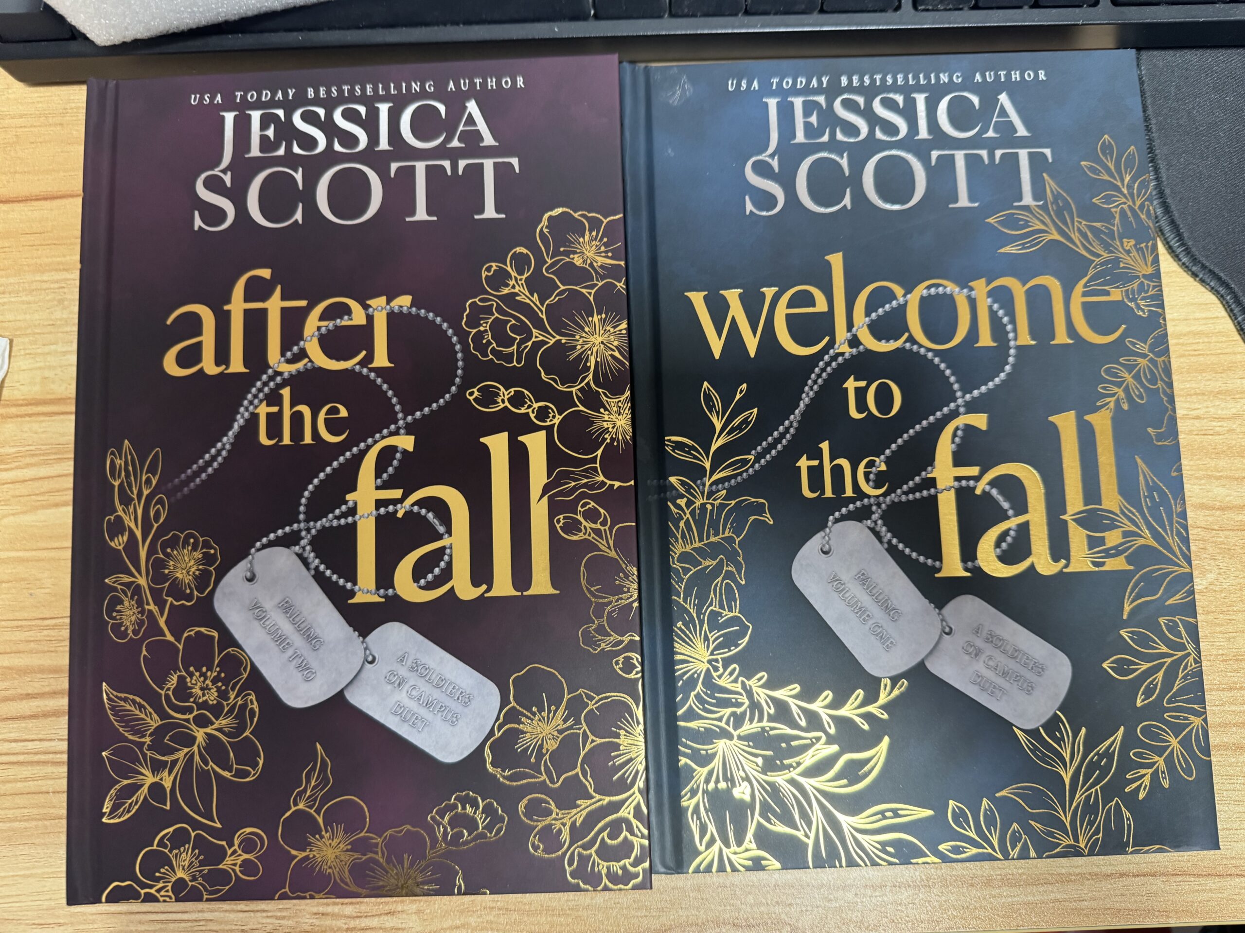 hardcover copies of Welcome to the Fall and After the Fall special edition. deep mauve and deep blue covers with gold letters and dog tags among flowers.